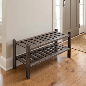 May include: A two-tier shoe rack constructed from dark brown wood with a weathered finish. The unit features four vertical corner posts and two horizontal slatted shelves designed for storage, standing on a light-colored wooden floor.