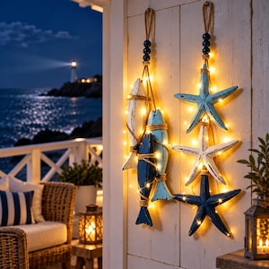 Peut inclure: Deux décorations murales verticales à motifs nautiques. Une guirlande présente trois poissons en bois blanc, bleu clair et bleu foncé, entourés de corde. L'autre guirlande montre trois étoiles de mer bleu clair, blanches et bleu foncé, éclairées par des guirlandes lumineuses.