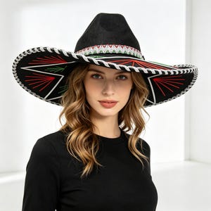 Peut inclure: Un chapeau noir à larges bords doté d'une bande décorative aux motifs géométriques rouges, blancs et verts. Le bord est fini avec une garniture métallique argentée, et le dessous présente une broderie en étoile rouge et verte sur fond noir.