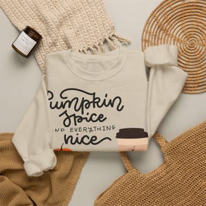 Könnte beinhalten: Ein cremefarbenes Sweatshirt mit Rundhalsausschnitt und dem schwarzen Text "Pumpkin Spice AND EVERYTHING nice" sowie einer Grafik einer Kaffeetasse und eines Kürbisses. Das Sweatshirt hat lange Ärmel sowie gerippte Bündchen an Kragen, Ärmeln und Saum.