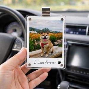 May include: A clear acrylic rectangular car hanging ornament featuring a photo of a tan Shiba Inu dog wearing a red harness sitting on a wooden bench in a field of orange flowers. The bottom white border displays the text I Love forever with a paw print.