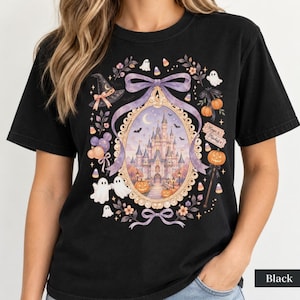 Op de afbeelding: Een zwart t-shirt met een grafische print van een kasteel in een sierlijk ovaal frame, omringd door lavendelkleurige strikken, spoken, pompoenen, een heksenhoed en maissnoepjes. De tekst "Magic & Mischief" staat op een klein rechthoekig bordje.