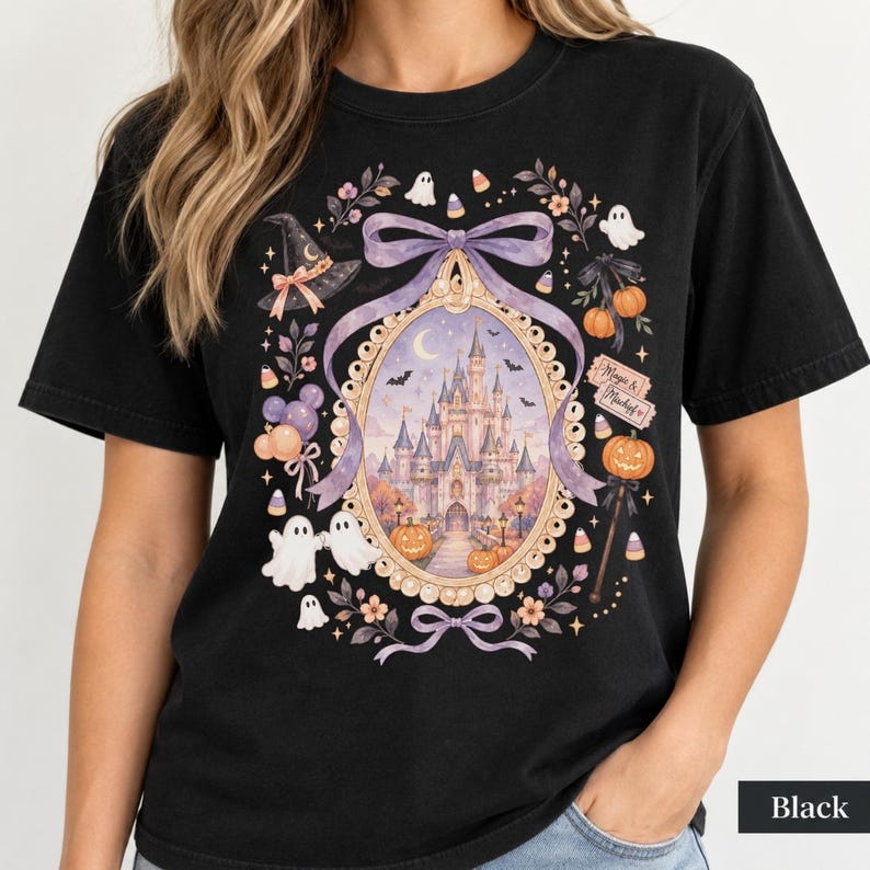 Op de afbeelding: Een zwart t-shirt met een grafische print van een kasteel in een sierlijk ovaal frame, omringd door lavendelkleurige strikken, spoken, pompoenen, een heksenhoed en maissnoepjes. De tekst "Magic & Mischief" staat op een klein rechthoekig bordje.