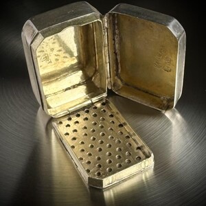May include: A rectangular silver box with a hinged lid and a removable interior grate featuring a grid of circular perforations. The interior surfaces are gold-toned, and the metal shows visible hallmarks stamped on the inner lid and base.