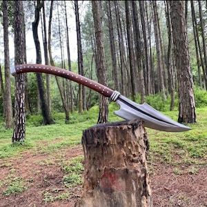 May include: A long-handled polearm featuring a curved dark brown wooden shaft adorned with a series of small silver-colored metal studs along its length and a sharp, pointed steel blade head with a central ridge and a distinct side notch.