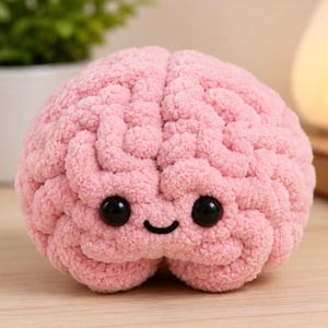 Può includere: Un peluche all'uncinetto di colore rosa chiaro a forma di cervello umano. Il filato testurizzato crea un aspetto superficiale dettagliato e pieghettato. Presenta due grandi occhi rotondi in plastica nera lucida e un piccolo sorriso nero ricamato.