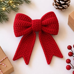 May include: A bright red crochet bow featuring a central knot and two long, pointed tails. The bow is constructed with a dense, uniform stitch pattern, creating a textured surface. The design is symmetrical, with wide loops on each side.