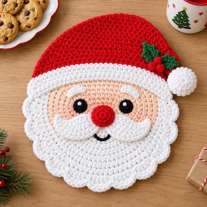 May include: A round, crocheted Santa Claus face coaster featuring a red hat with a white pom-pom and green holly leaves with red berries. The face has a peach-colored skin tone, black eyes, a red nose, and a white crocheted beard and mustache.