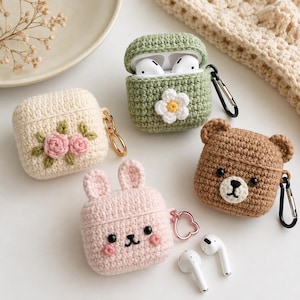 Puede incluir: Cuatro fundas de ganchillo para AirPods: una verde con flor blanca, una crema con rosas rosadas, una de conejo rosa claro con orejas y una de oso marrón con orejas. Cada funda incluye un mosquetón o anillo de metal para sujeción.