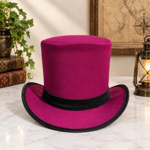 May include: A vibrant magenta top hat featuring a flat crown and a wide, curved brim. The base of the crown is encircled by a solid black velvet ribbon band, and the outer edge of the brim is finished with a matching black trim.