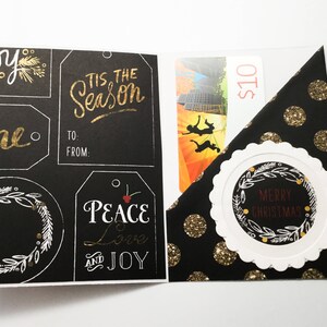 May include: A Christmas gift card holder. The black card has gold glitter polka dots and a white scalloped circle with "MERRY CHRISTMAS" text. The left side has tags with "TIS THE SEASON" and "PEACE LOVE AND JOY" text.