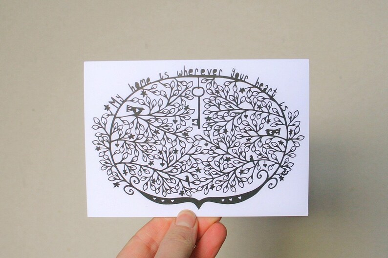 May include: A white card with a black illustration of a tree with leaves, birds, stars, and a key. The text "My home is wherever your heart is" is written around the top of the tree design.