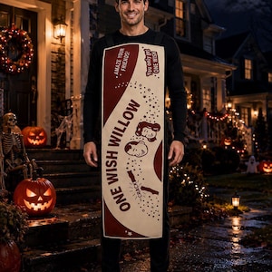 K&ouml;nnte beinhalten: Ein rechteckiger Kost&uuml;m-Tabard mit einem cremefarbenen und kastanienbraunen Design mit dem Text ONE WISH WILLOW, AMAZE YOUR FRIENDS! und You only get ONE WISH. Die Grafik enth&auml;lt Illustrationen von zwei Gesichtern und einem Wunschknochen mit dem Wort CRACK.