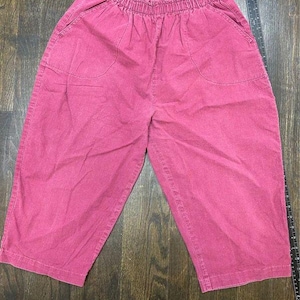 May include: Solid dark pink cropped pants featuring an elasticized waistband with a ruffled edge, two side pockets, and a straight-leg cut. A black ruler is positioned along the right side, showing the garment length is approximately 28 inches.