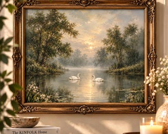 May include: A landscape painting in an ornate gold frame depicting two white swans swimming on a calm lake at sunset. The scene features lush green trees, soft golden light reflecting on the water, and a hazy, tranquil atmosphere in the background.