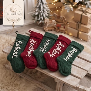 Puede incluir: Cinco calcetines navideños de punto trenzado en colores verde oscuro y rojo intenso, cada uno con un nombre bordado en blanco: Robert, Heather, Monica, Ashley y Parker. Los calcetines tienen un puño acanalado y un lazo para colgar.