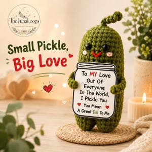 Könnte beinhalten: Ein grünes, gehäkeltes Gewürzgurken-Stofftier mit schwarzen Augen und rosa Wangen, das ein weißes Schild in Glasform hält. Der Text lautet: To MY Love Out Of Everyone In The World, I Pickle You You Mean A Great Dill To Me mit zwei roten Herzen.