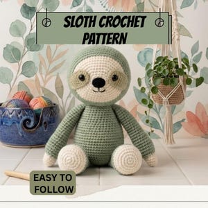 Può includere: Un bradipo giocattolo all'uncinetto con corpo verde salvia e viso, mani e piedi color crema. Il bradipo ha occhi e naso neri. Il testo sull'immagine recita SLOTH CROCHET PATTERN e EASY TO FOLLOW. Sono presenti una ciotola per lana blu e una pianta.