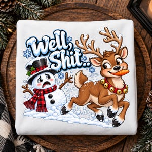 May include: A white sweatshirt featuring a graphic print of a cartoon snowman wearing a black top hat and red plaid scarf, and a brown reindeer with a red jingle bell collar holding a carrot in its mouth, with the text Well, Shit.. above them.