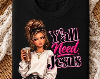 May include: A black sweatshirt featuring a graphic of a person with a high bun hairstyle, sunglasses, and a gold necklace, holding a coffee cup. The text Y'ALL NEED JESUS is printed in large, stylized pink and black lettering next to the illustration.