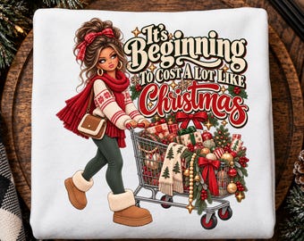 May include: A white sweatshirt featuring a graphic of a person with brown hair wearing a red scarf, white sweater, and tan boots, pushing a shopping cart filled with Christmas gifts, ornaments, and greenery, with the text It's Beginning To Cost A Lot Like Christmas.