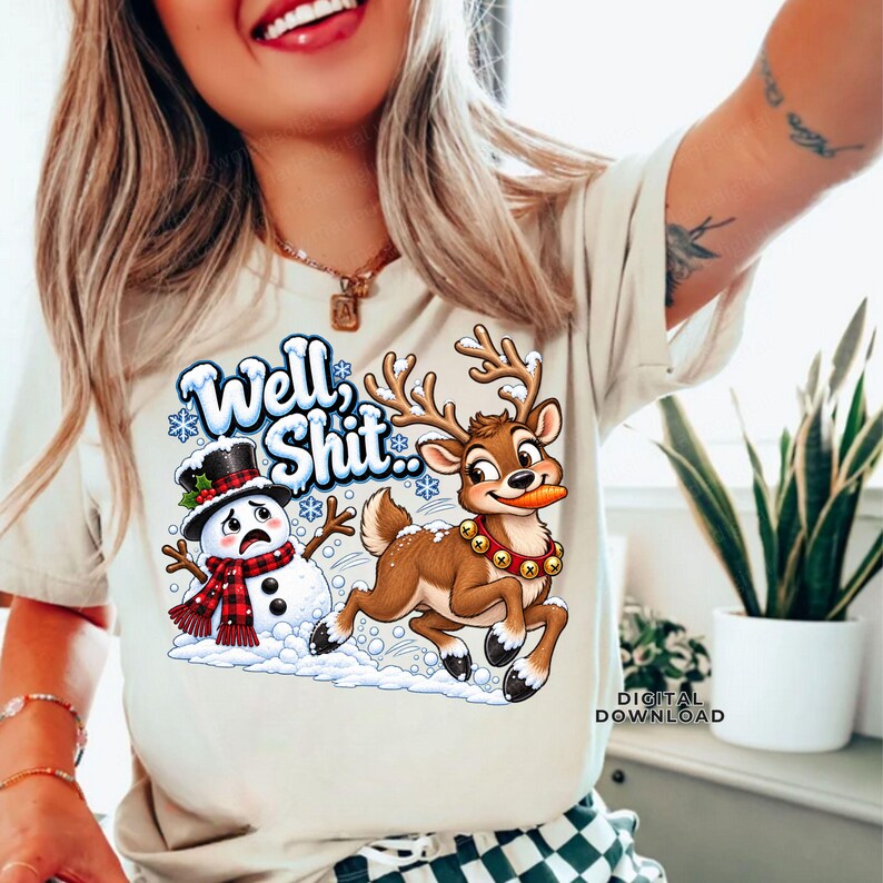 May include: A beige t-shirt featuring a graphic of a snowman wearing a black top hat and red plaid scarf, and a brown reindeer with a bell collar holding a carrot. The text "Well, Shit.." is printed in blue above the characters with snowflakes.