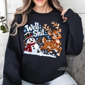 May include: A black long-sleeve sweatshirt featuring a graphic of a startled snowman wearing a red and black plaid scarf and a top hat, alongside a reindeer with a carrot in its mouth, with the text "Well, Shit.." in blue and white letters.