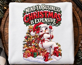 May include: A white sweatshirt featuring a graphic of a snowman wearing a Santa hat, red scarf, and red high-heeled boots, posing on a pole. The text reads, "MIND YA BUSINESS CHRISTMAS IS EXPENSIVE" above a decorated Christmas tree and gifts.