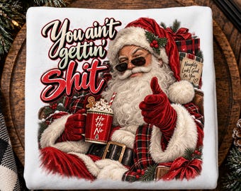 May include: A white sweatshirt featuring a graphic of Santa Claus wearing sunglasses and red gloves, holding a red mug with the text Ho Ho Ho. The text You ain't gettin' SHIT is printed above Santa, and a tag reads Naughty Looks Good On You.