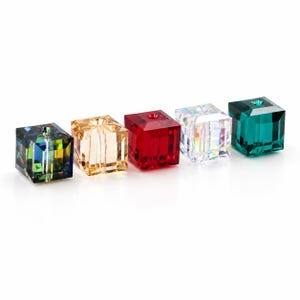 Può includere: Cinque perline sfaccettate a forma di cubo disposte in fila. Le perline sono colorate in blu scuro iridescente, oro chiaro, rosso intenso, trasparente con riflessi arcobaleno e verde smeraldo scuro. Ogni perlina presenta un foro centrale.