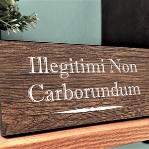 May include: A wooden sign with the Latin phrase "Illegitimi Non Carborundum" in white lettering. The sign has a dark brown wood grain finish.