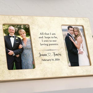 May include: A double photo frame with a beige background and a gold trim. The frame has two openings for photos. The top opening has a quote about loving parents. The bottom opening has the names Jenna and Travis and the date February 14, 2024.
