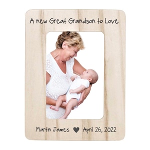 May include: A light-colored wooden picture frame with the text "A new Great Grandson to Love" at the top. The frame holds a photo of a baby being held by a woman. The text "Martin James" and "April 26, 2022" are at the bottom.