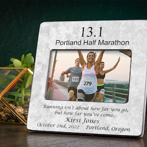 May include: A white marble photo frame with a black mat and a photo of runners in a race. The frame has the text "13.1 Portland Half Marathon" and "Running isn't about how far you go, but how far you've come. Kirsi Jones October 2nd, 2022 Portland, Oregon".