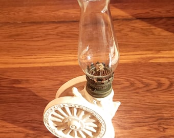 May include: White ceramic oil lamp shaped like a wagon wheel with a clear glass chimney.