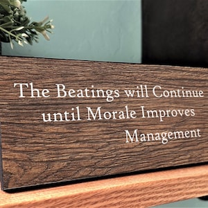 May include: A wooden sign with the text "The Beatings will Continue until Morale Improves Management".