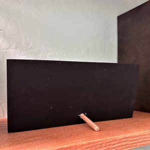 May include: A small black chalkboard with a wooden stand. The chalkboard is blank and ready to be written on.