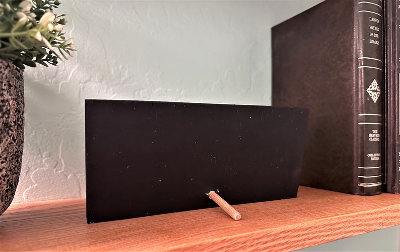 May include: A small black chalkboard with a wooden stand. The chalkboard is blank and ready to be written on.
