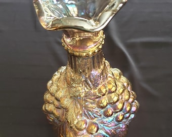 Può includere: Una decanter in vetro iridescente vintage con un motivo a grappolo d'uva. La decanter ha una parte superiore larga e svasata e un corpo rotondo con un designo a grappolo d'uva dettagliato.