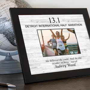 May include: A black framed photo with a white woodgrain background. The photo shows a woman running a half marathon with the text "13.1 Detroit International Half Marathon" and "She believed she could. And she did. October 20, 2024 1:49:48 Aubrey Wood".