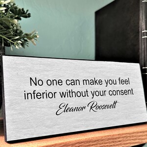 May include: A white desk plaque with black text that reads "No one can make you feel inferior without your consent - Eleanor Roosevelt".