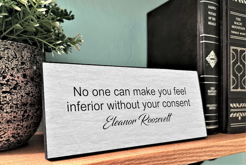 May include: A white desk plaque with black text that reads "No one can make you feel inferior without your consent - Eleanor Roosevelt".