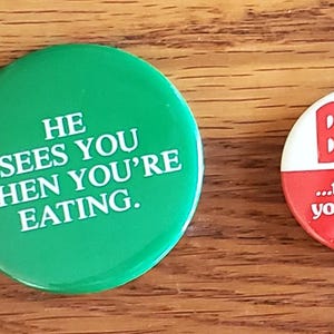 May include: A collection of four vintage pinback buttons. One white rectangular button features a black illustration of a building with the word "ONTARIO". A green button reads "HE SEES YOU WHEN YOU'RE EATING". A red button says "BEEF...the food you're right to like". A white button has a purple cat and text.