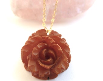 May include: A gold chain necklace with a carved brown rose pendant. The rose is detailed and has a swirl pattern in the center.