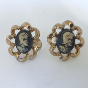 May include: A pair of gold tone earrings with a black and white cameo of a man in a helmet. The cameo is set in a flower-shaped design.