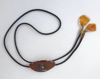 May include: A brown agate bolo tie with a black cord and two smaller agate pieces at the ends.