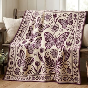 May include: A cream-colored crochet blanket featuring a repeating pattern of dark purple butterflies, tulips, and daisies. The design includes a decorative border with small flowers and vines, creating a cohesive botanical motif.