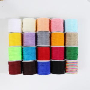 Puede incluir: Una colección de veinte carretes de cordón de nailon dispuestos en una cuadrícula. Los colores incluyen blanco, crema, melocotón, rosa, azul claro, amarillo, lavanda, gris, naranja, beige, verde lima, turquesa, rojo, magenta, verde oscuro, granate, marrón, azul, negro y arcoíris.