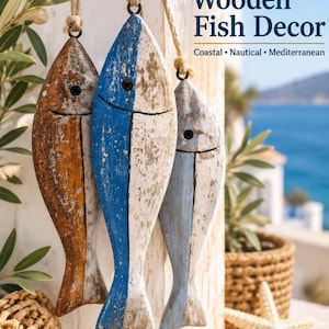 Peut inclure: Trois poissons décoratifs en bois suspendus avec une finition peinture vieillie en marron, bleu et bleu clair. Chaque poisson présente un œil et une bouche sculptés, suspendus par une corde de jute. Le texte Wooden Fish Decor Coastal Nautical Mediterranean est visible.