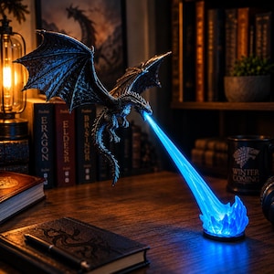 May include: A dark, textured dragon figurine in flight, emitting a bright blue light beam from its mouth that illuminates a base of blue flames. The dragon is suspended in mid-air, featuring detailed wings and scales, creating a glowing effect.